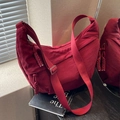 Deep red nylon crescent crossbody bag with woven knot zipper detail on a book - Red