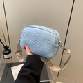 Light blue embossed square crossbody bag with ethnic woven strap held by a model - Blue