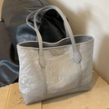 Chic grey tote bag with pleated texture and gold logo plaque on a black leather sofa - Silver
