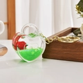 Dettaglio di un portachiavi liquido a forma di cuore con rosa rossa e glitter verdi - Catena Oro Chiaro + Serratura Cuore Rosa / Verde