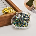 Close-up of a heart-shaped acrylic liquid keychain with star sequins and golden bell - Light Gold Chain + Luminous Heart + Bell / Grey Black