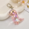 Detailed shot of iridescent acrylic dinosaur keychain with silver hardware on white tray - Pink