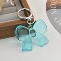 Detail of teal translucent acrylic bow keychain with silver ring on a soft tray - Blue