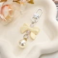 Close-up of cream resin bow keychain with large faux pearl and white lobster clasp - Off White