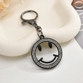 Macro shot of gun-black smiley face keychain with micro-pave white rhinestones on white tray - Keychain + Pendant / Smiley Face Black