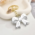Silver bow keychain with gold ring and engraved heart tag on white tray - White