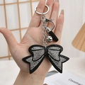 Detail of a black bow keychain with white rhinestones and fringe, held in hand - Black Edge with White Rhinestone