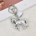 Silver metal horse keychain with white bell detail on a soft plush surface - Silver