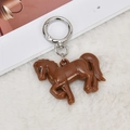 Macro detail of brown acrylic pony charm with metallic silver key ring on soft white fur - Brown