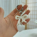 Close-up of a white resin bow and heart-shaped pendant keychain held in hand - Silver Ring + Heart + Bow / Off White