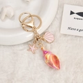 Detail view of gold keychain with starfish and shell pendants on soft white fabric - Orange
