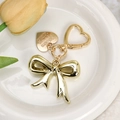 Close-up of a gold bow keychain with heart clasp and heart charm on a ceramic tray - Gold Bow with Engraved Tag