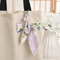 Floral bow keychain with pearl chain and purple mini bag charm on beige tote - Violet