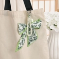 Floral silk bow and pearl strap keychain with mint mini bag charm on a white canvas bag - Fruit Green
