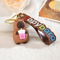 Cute capybara keychain holding bubble tea with a brown strap on decorative background - Letter Strap And Capy / Milk Tea