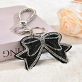 Close-up of bow keychain with black and silver rhinestones on soft plush background - White Edge with Black Rhinestone