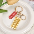 Golden mini abacus keychain with red tag and lobster clasp on a white plate - Pass Every Exam
