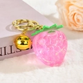 Pink resin strawberry keychain with golden bell and lobster clasp on white plush background - Pink With Bell