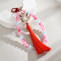 Detail of pink beaded phone charm featuring a golden cat silhouette and red tassel - Rose Red