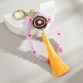 Macro shot of evil eye keychain with purple beads, flower charm, and bright yellow tassel - Purple