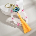 Handmade Evil Eye keychain with blue beads, pink flower charm, and yellow tassel pendant - White