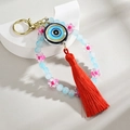 Macro view of blue evil eye keychain with pink flower beads and vibrant red silk tassel - Blue