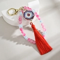 Macro detail of handmade evil eye keychain with pink beads and bright red silk tassel charm - Rose Red