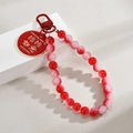 Detail of red beaded keychain with gold engraved metal tag showing auspicious characters - Persimmon
