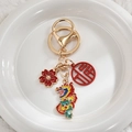 Golden dragon keychain with red enamel flower and lucky Fu pendant on a white ceramic plate - Double Dragons