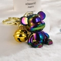 Close-up of iridescent gradient bear keychain with golden bell on plush background - Iridescent Gradient