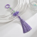 Détail du pendentif à pompon en soie violette avec perles vertes et fleurs sur plat blanc - Anneau Coloré + Chaîne + Gland / Violet