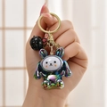 Detail of iridescent rabbit keychain featuring golden ring and black bell accessory - Grey Rabbit