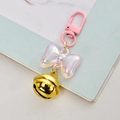 Pink bow pendant keychain with iridescent pearl finish and gold bell charm on blue background - Pink With Bell