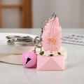 Macro shot of a pink resin envelope keychain with Fly gold lettering and a bell accessory - Feather Design / Pink Free