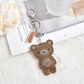 Détail macro du porte-clés ours en strass marron et blanc avec frange et clochette argent - Or