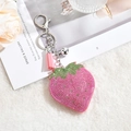 Detailed view of strawberry rhinestone keychain with pink tassels and silver bell on white fur - Keychain + Rhinestone Pendant / Pink with Green Leaf (Tassel Style)