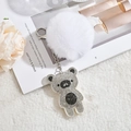 Sparkling rhinestone bear keychain with a fluffy white faux fur pompom on a magazine - White