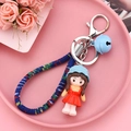 Detail of cute doll keychain with woven rope and bell on a pink decorative tray - Red