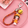 Detail of cute resin doll keychain with orange woven rope and yellow bell on pink tray - Lemon Yellow
