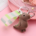 Close-up of brown flocked dinosaur keychain with green spikes and striped ribbon strap - Brown