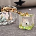 Porte-clés cube en acrylique avec lapin mignon et chaîne dorée sur fond texturé gris - Vert