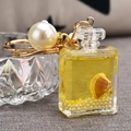 Detail view of perfume bottle keychain with yellow quicksand, pearl and gold clasp - Gold