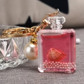 Detalle macro del llavero de frasco de perfume acrílico con líquido rosa, concha y perla - Rosa Roja