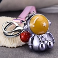 Macro view of silver astronaut keychain with yellow star helmet and red bell charm detail - Purple