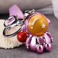 Close-up of metallic pink astronaut keychain with red bell and pink wrist strap accessory - Pink