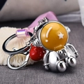 Close-up of astronaut keychain with silver metal finish, red bell, and translucent wrist strap - White