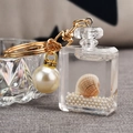 Detail of acrylic perfume bottle keychain with gold hardware, shell, and pearls - White