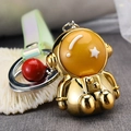 Detailed view of a shiny gold astronaut keychain with a red bell and iridescent strap - Gold