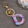 Detail view of resin letter D keychain with colorful stones, gold ring and small bell - Letter D