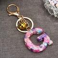 Macro shot of resin letter G keychain with colorful polished stones and gold bell detail - Letter G